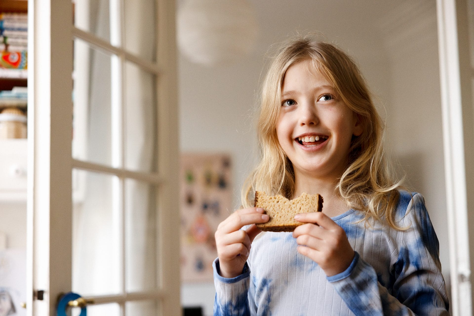 Kid holding a piece of bread with seems fresh and delicious with bites taken out of it.