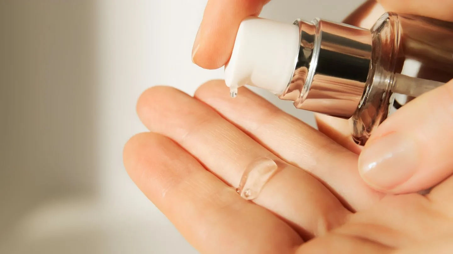 A close-up of a hand dispensing a clear gel from a pump bottle onto the palm of another hand.