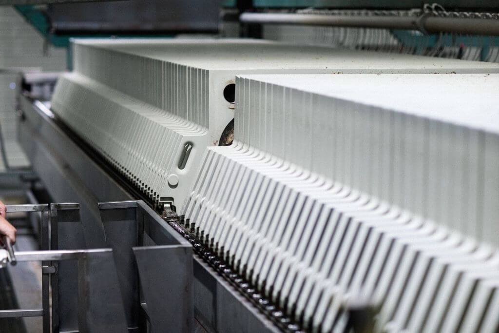 Close-up view of an industrial brewing filter press with multiple ridged plates and metal components in the background