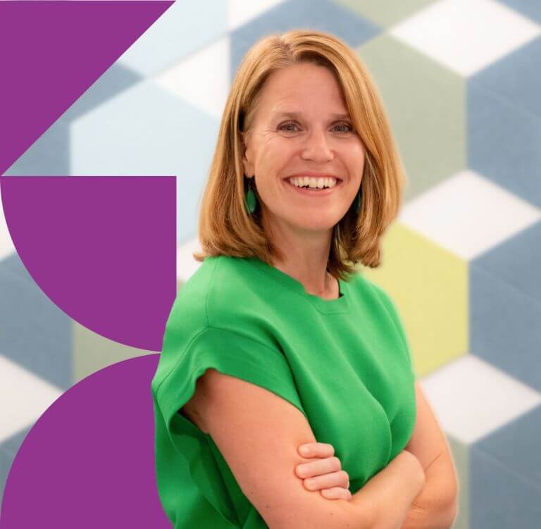woman with red hair in a green top with arms crossed, standing in front of a geometric background with hexagonal patterns and purple graphic elements.