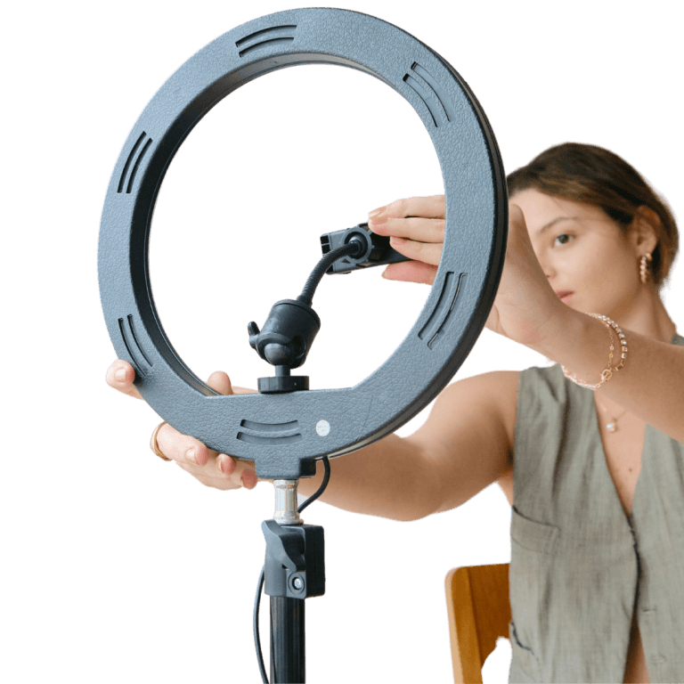 A person seated on a wooden chair adjusts a ring light on a stand, preparing for digital content creation.