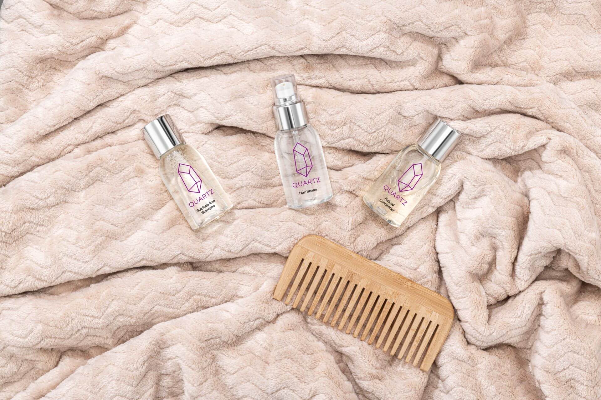 Three bottles of Quartz haircare products and a wooden comb placed on a soft, beige, textured blanket.
