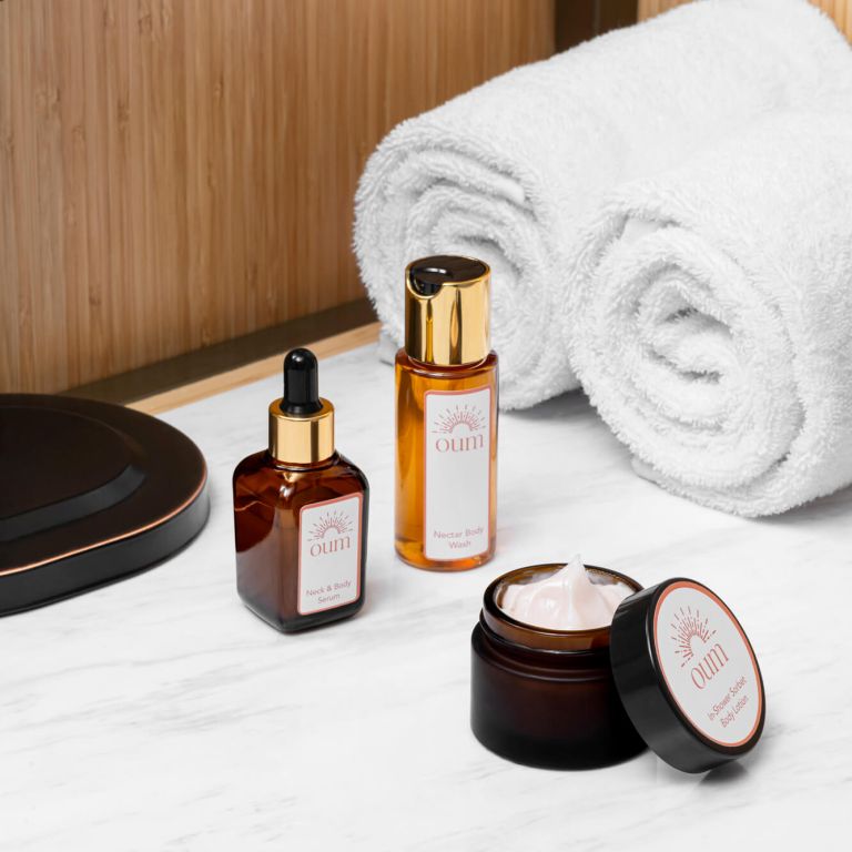 A bathroom countertop with three bodycare products from IFF's cosmetic formulation Oum. The products include a dropper bottle labeled 
