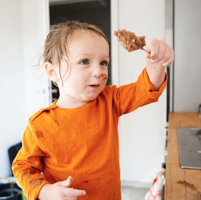 Child in an orange shirt holding an item in a kitchen setting, with text about PREFERENZ® M 200 enzyme.