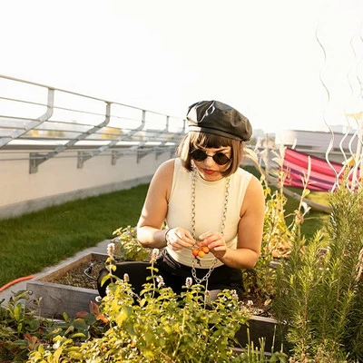 Young, millennial woman sitting outdoors with plants on a urban rooftop, sustainable garden.