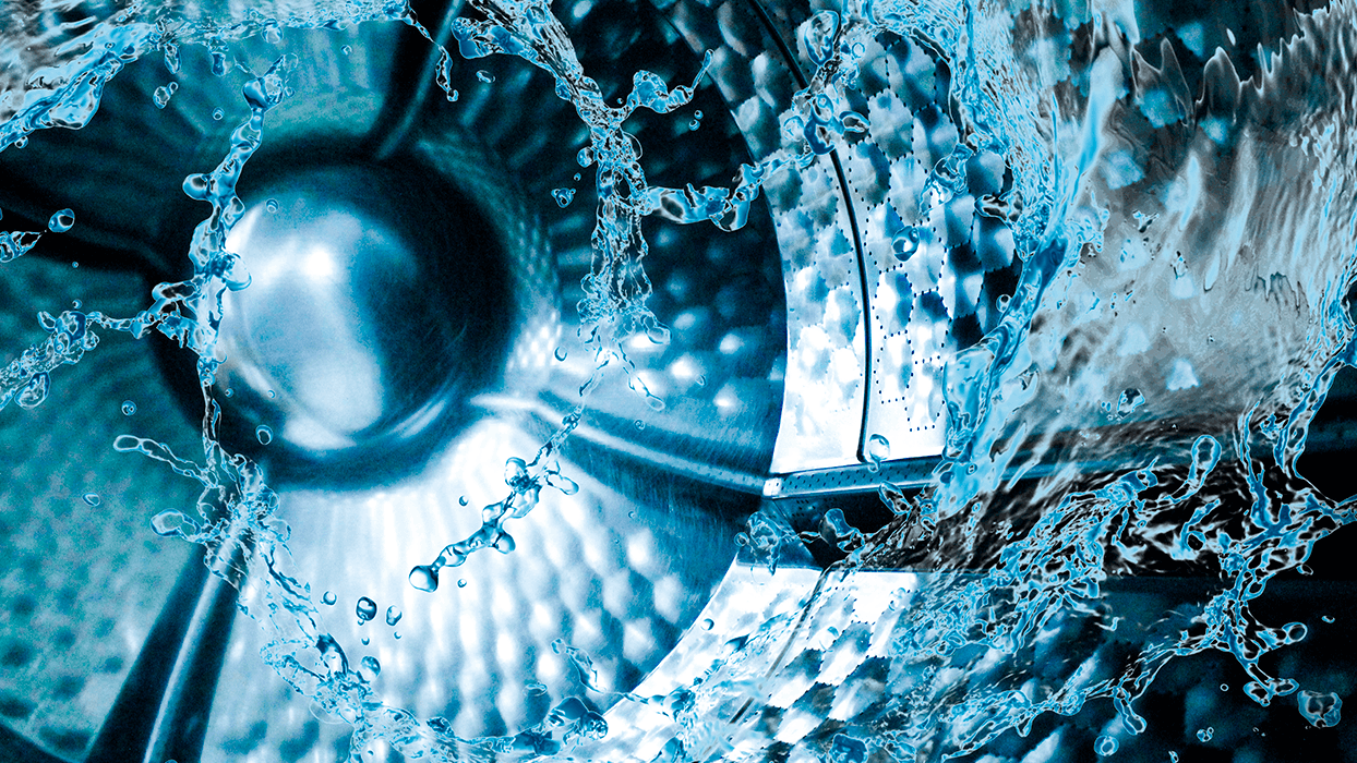 Inside view of a washing machine drum with water splashing around, highlighting the use of sustainable laundry enzymes.