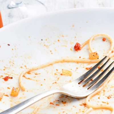 A close-up of a dirty white plate with remnants of spaghetti and sauce, along with a fork.