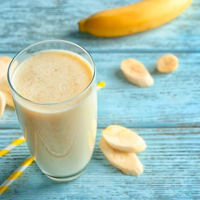 A glass of banana protein smoothie on a wooden table with banana in the background.