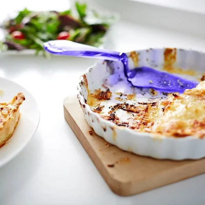 A white ceramic dish with baked-on protein stains being scraped clean with a purple spatula, showcasing the effectiveness of sustainable dishwashing enzymes.