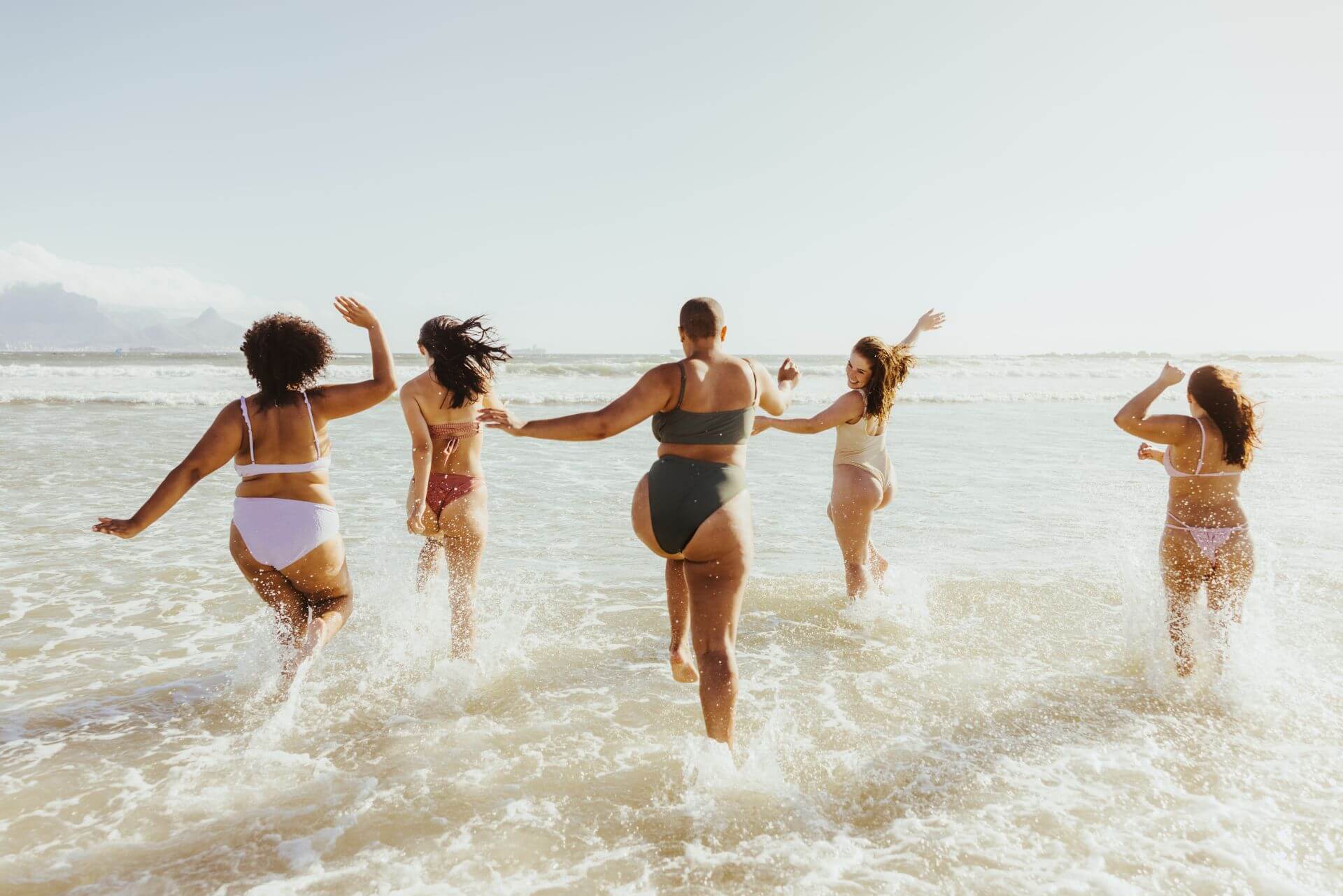 No Filter formulation collection. Five people in swimsuits running into the ocean waves on a sunny day.