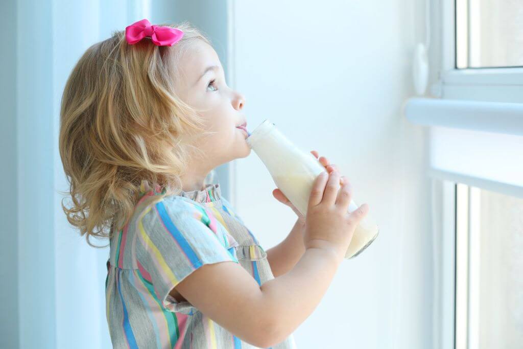 kid with a drinkable yogurt looking at a window