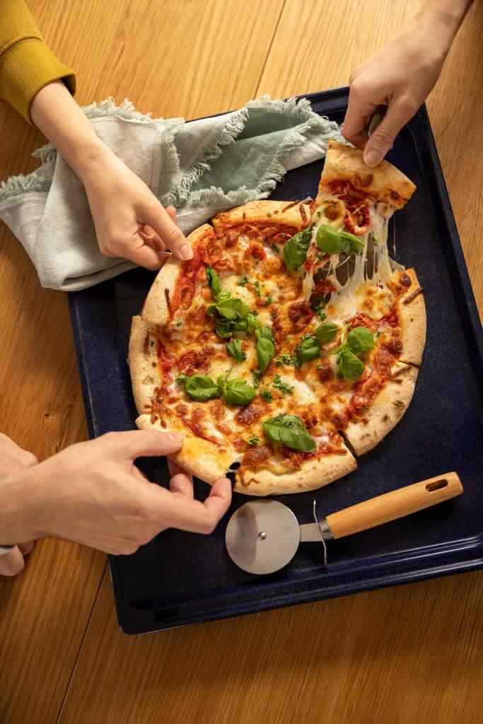Pizza with melted cheese on platter with 3 people taking a slide with their hands