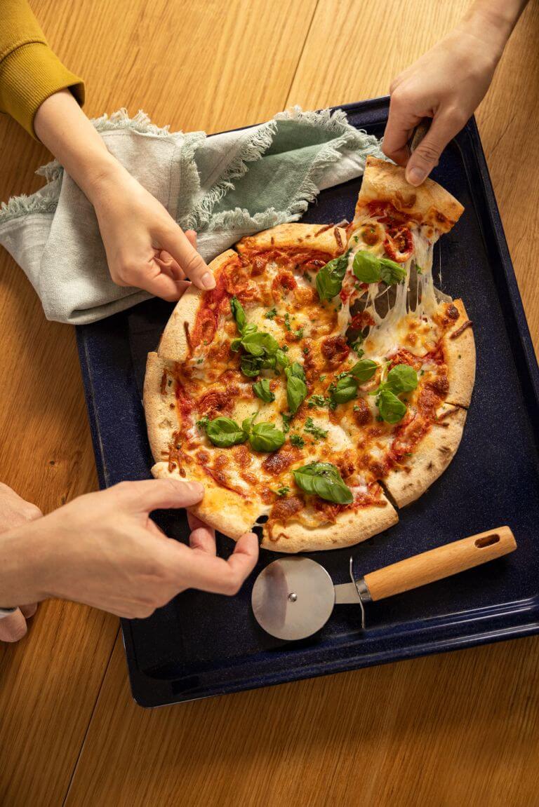 Pizza with melted cheese on platter with 3 people taking a slide with their hands