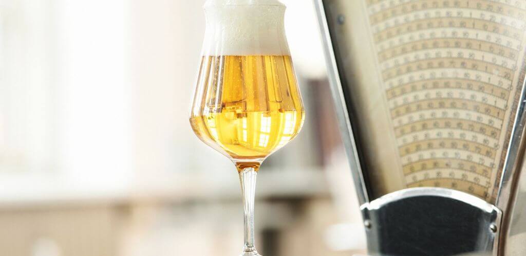 Glass of beer with a frothy head next to an industrial scale