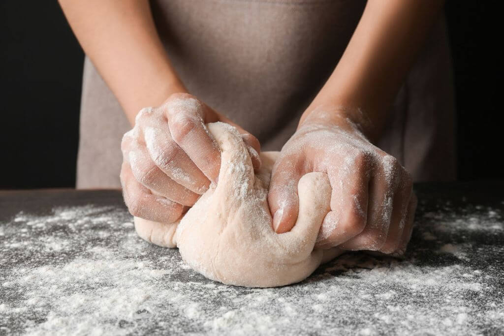 Hands kneading dough on a floured surface. IFF's GRINDAMYL™ range of baking enzymes providing a wide range of benefits like dough strength, flour correction and flour and bread performance.