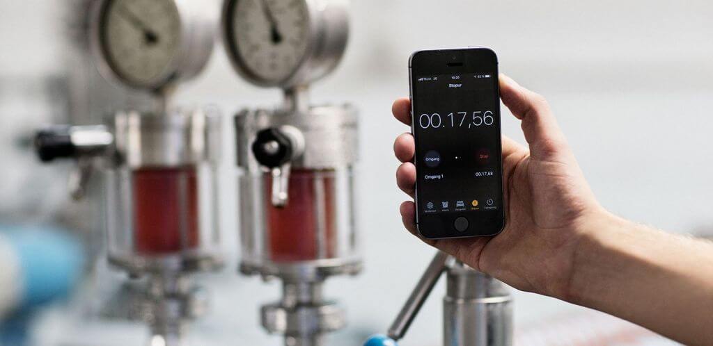Hand holding a smartphone with a stopwatch app,, in front of industrial pressure gauges and equipment