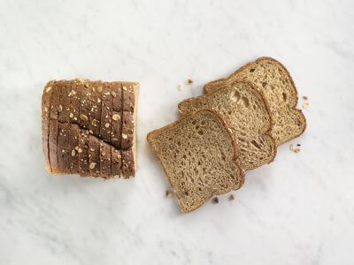 A loaf of sliced multigrain bread on a marble surface with several slices separated and laid out to the right. POWERFRESH® enzymes for baked goods freshness.