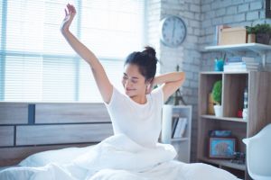 Woman in white clothes stretching and waking up in her bedroom