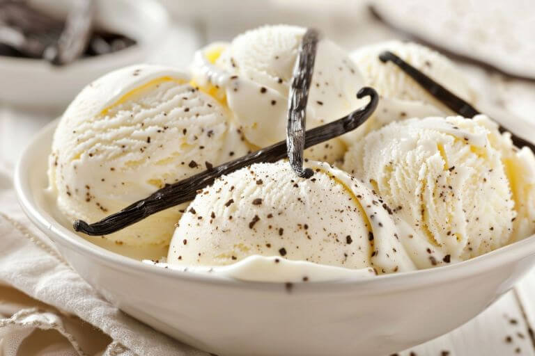 Vanilla bean ice cream in a white bowl with vanilla beans on top and in the background.