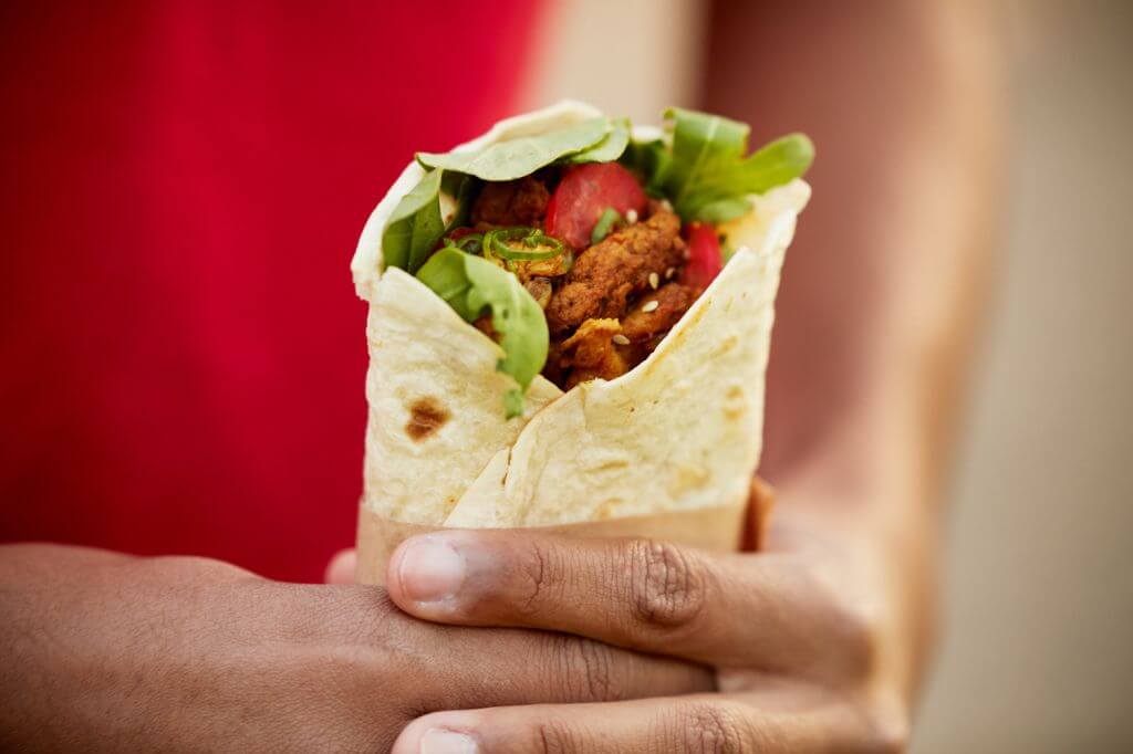 Close-up of hands holding a wrap filled with greens and seasoned meat or vegetables