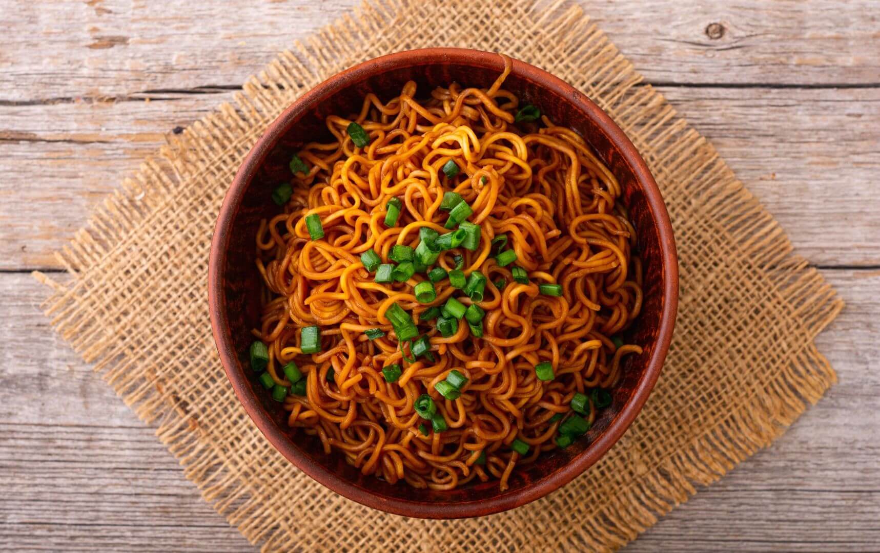 Bowl of noodles with seasoning, sitting on a wooden table