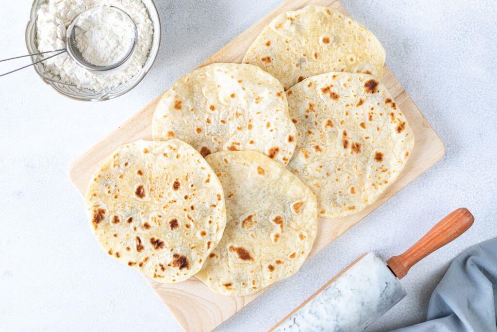 Four freshly cooked tortillas on a wooden cutting board