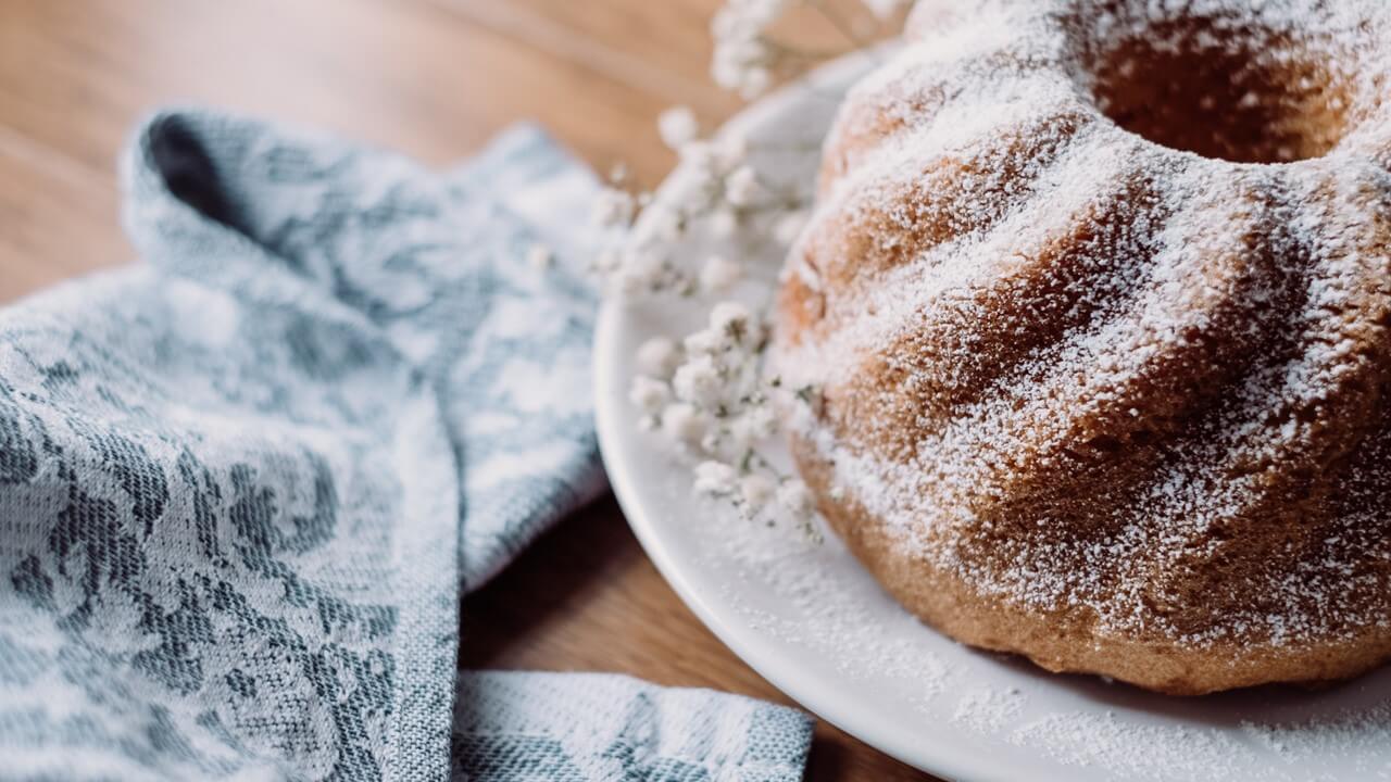 A close-up of a cake covered with powdered sugar on a white plate. Cakes using POWERSOFT® enzymes for anti-staling