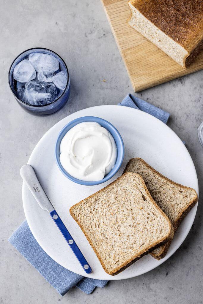 Two slides of baked whole grain bread with cream next to it