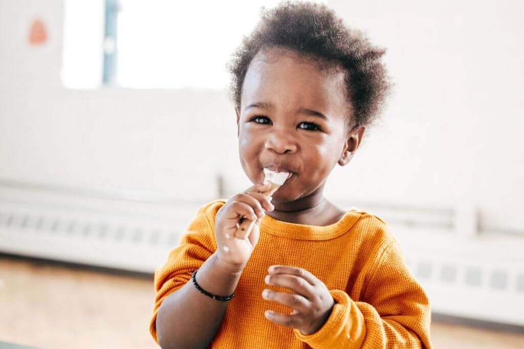 Child with a spoon on his hands eating yogurt or fresh fermented product