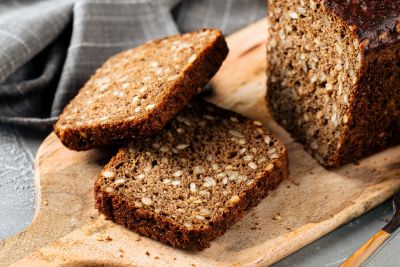 Several slices of whole grain bread arranged in a semi-circle on a wooden cutting board. Wheat stalks are placed near the cutting board.