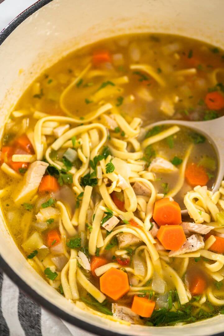 Close-up photo of a bowl of noodles with vegetables, seasonings and broth being scooped by a spoon