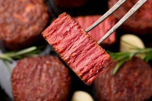 Fork holding up plant-based meat that looks like felt mignon that's been sliced in half. More rounds of plant-based meat in background
