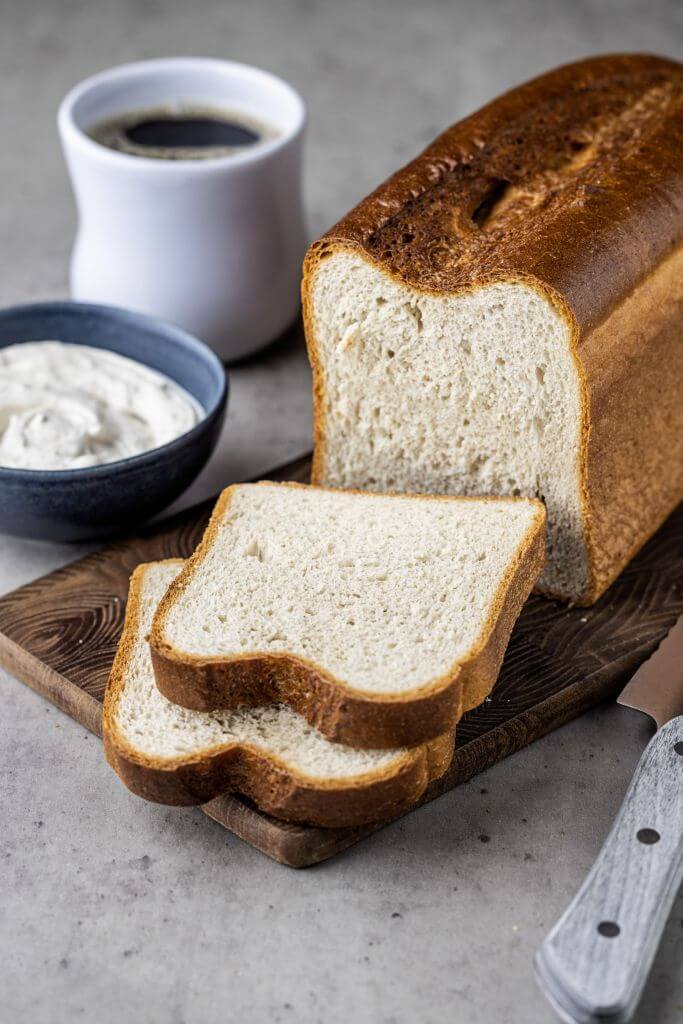 A loaf of bread with two slices cut from it, placed on a wooden cutting board