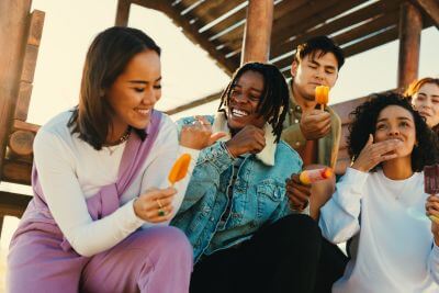 Diverse group of young adult friends, sitting under a dock and eating different product-reformulated ice cream treats