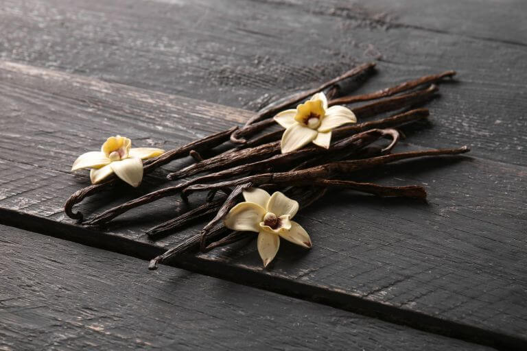 A stack of vanilla beans and vanilla flowers sitting in a bunch on top of a dark wooden table