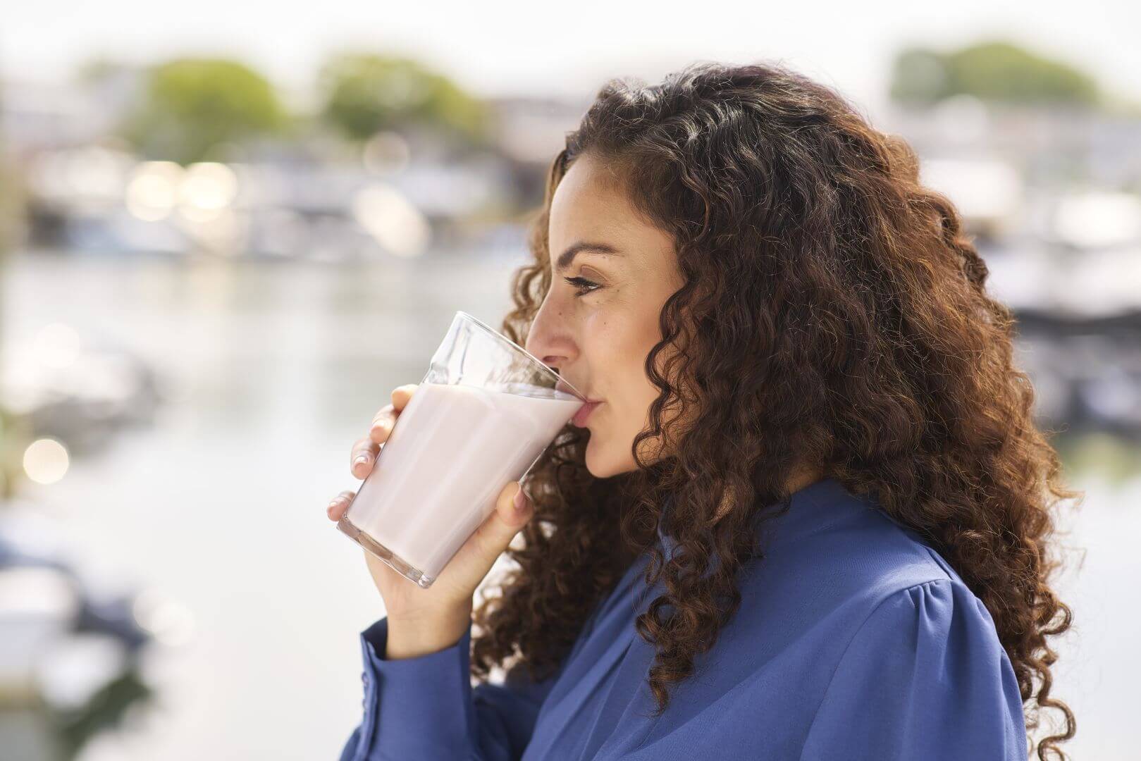 Side profile of a woman with dark curly hair and a blue shirt drinking a drinkable yogurt beverage