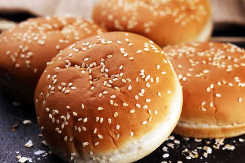 Close-up of golden sesame seed hamburger buns arranged together on a dark surface