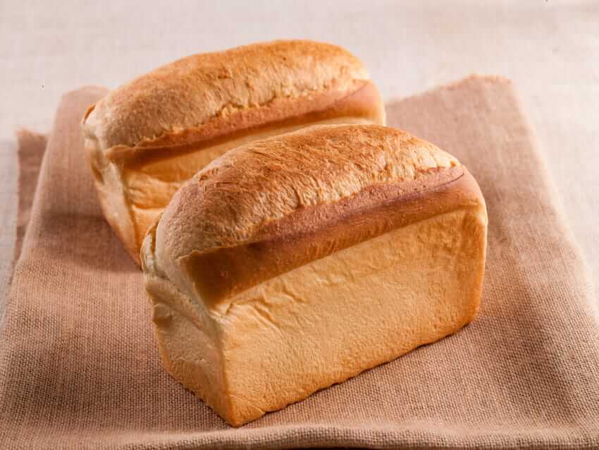 Two freshly baked golden loaves of white bread sitting on a burlap cloth